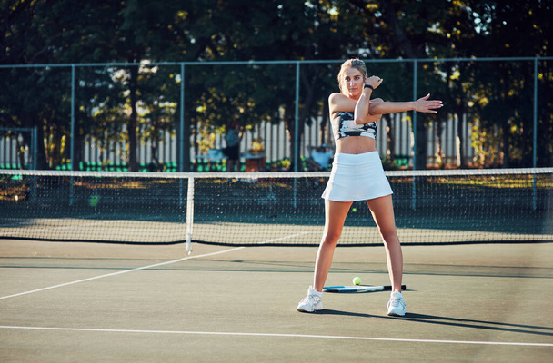Doskonałość jest stopniowym rezultatem ciągłego dążenia do poprawy. sportowa młoda kobieta rozciągająca ramiona podczas treningu na korcie tenisowym - Zdjęcie, obraz