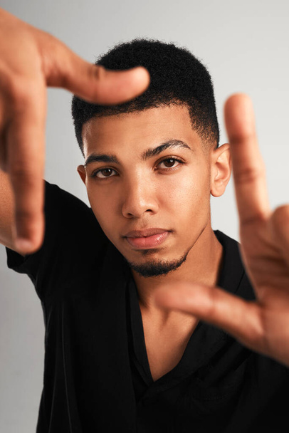 Frame by frame. Portrait of a handsome young man making a frame with his fingers while standing against a grey background inside of a studio - Fotoğraf, Görsel