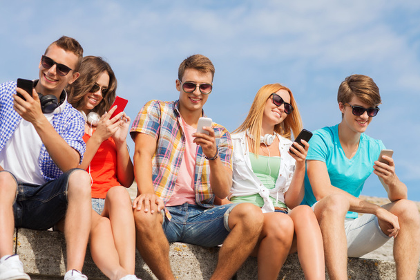 grupo de amigos sonrientes con teléfonos inteligentes al aire libre
 - Foto, imagen