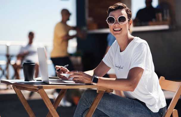 Vaihdan vain kuulumisia. Muotokuva iloinen nuori nainen työskentelee hänen kannettava tietokone, kun istuu pöydässä vieressä ranta kävelykatu ulkona päivällä - Valokuva, kuva