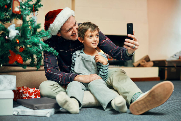 Kerstochtend met mijn kleine kerel. een schattig jongetje neemt selfies met zijn vader terwijl het uitpakken van kerstcadeaus thuis - Foto, afbeelding