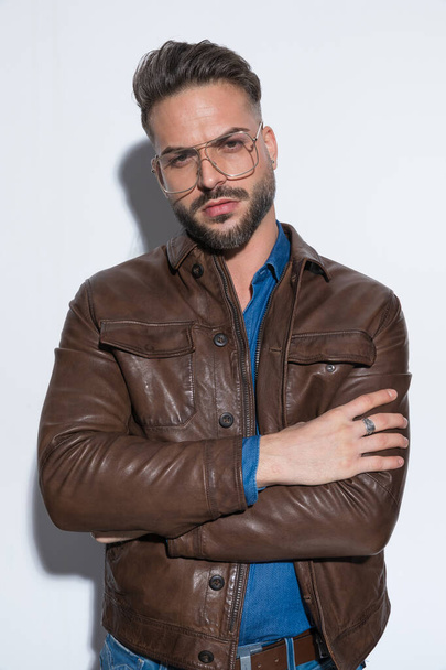 Attractive casual man with tough attitude is crossing his arms, looking at the camera, wearing eyeglasses against white studio background - Zdjęcie, obraz