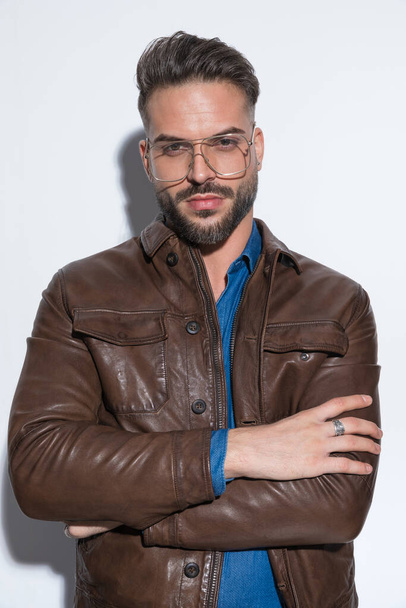 Handsome casual man is crossing his arms at chest and wearing glasses against white studio background - Foto, afbeelding