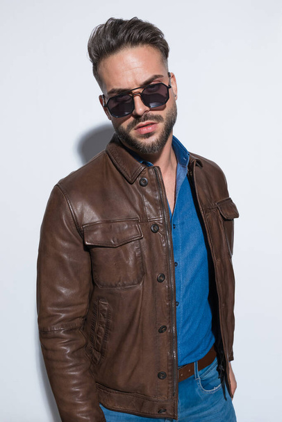 クールなサングラスを身に着けているカジュアルな男とファッション写真白いスタジオの背景に対する茶色の革のジャケット - 写真・画像