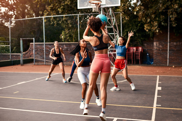 Με κάνει να δουλεύω σκληρά για την βολή μου. μια ποικιλόμορφη ομάδα αθλητριών που παίζουν ένα ανταγωνιστικό παιχνίδι μπάσκετ μαζί κατά τη διάρκεια της ημέρας - Φωτογραφία, εικόνα