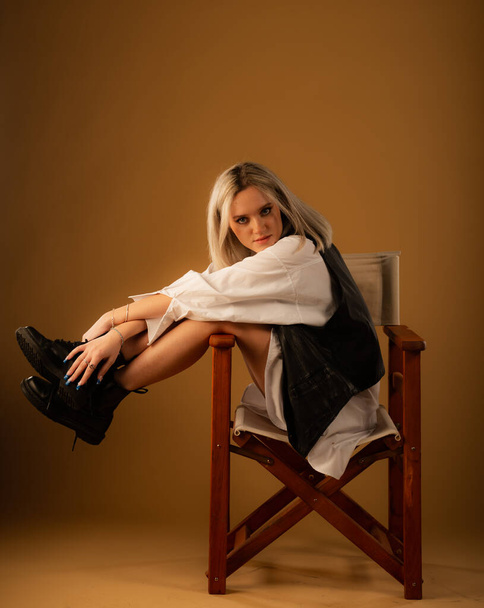 Atrakcyjne i niesamowite młoda dziewczyna jest pozowanie na krześle sam w studio na żółtym tle podczas zabawy - Zdjęcie, obraz