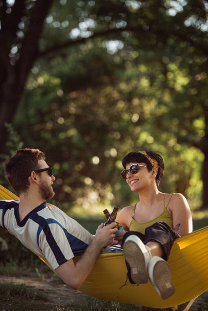 Beau couple parlant et se relaxant sur un hamac jaune dans le parc - Photo, image