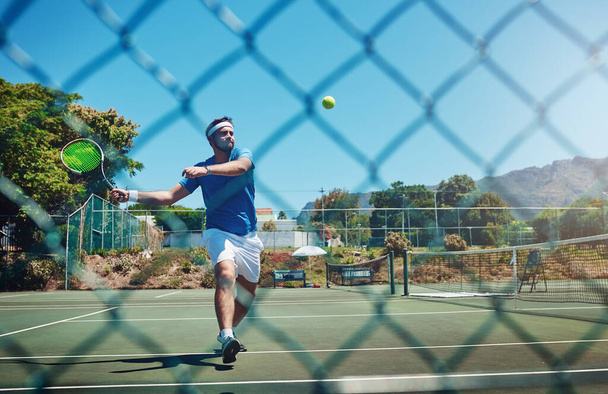 Pushing myself to my limits. Full length shot of a handsome young sportsman playing tennis alone on a court during the day - Photo, Image
