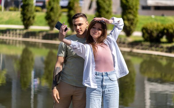 Image of a happy young beautiful loving couple posing walking outdoors in park nature take selfie by mobile phone - Fotó, kép