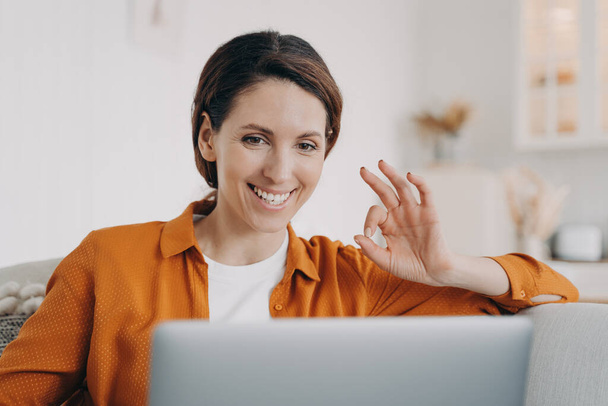 Mosolygó spanyol nő videóhívással beszél a laptopon, egyetért a barátjával, igen gesztust mutat. Happy female freelance worker makes okay sign, jóváhagyja az ügyfél feladatát, elfogadja a projektet. - Fotó, kép