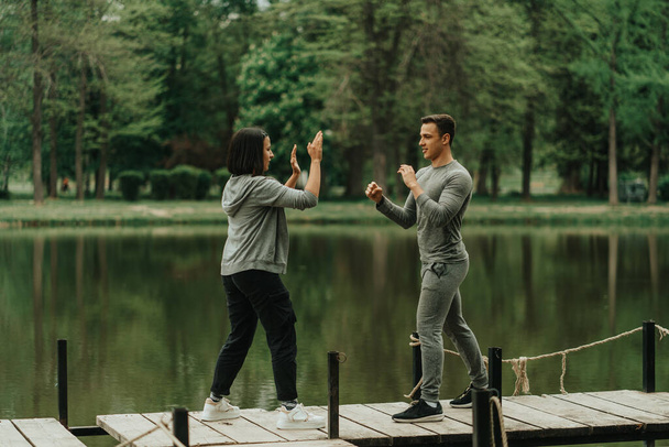 Jóképű fiú bokszol a barátnőjével, miközben a hídon áll a parkban. - Fotó, kép