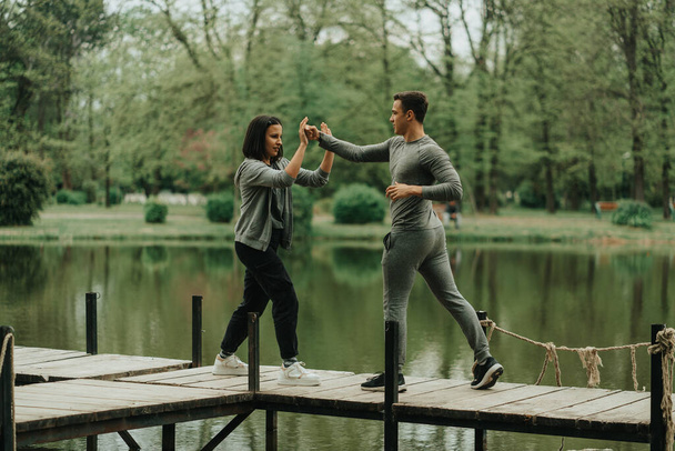 Hermoso boxeador haciendo ejercicio con su chica mientras está de pie en el puente en el parque - Foto, Imagen