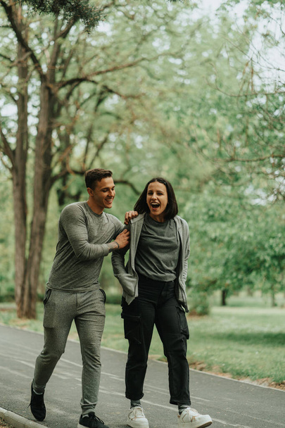 公園の道を歩いている間に楽しそうに笑っている美しいスポーツカップル - 写真・画像
