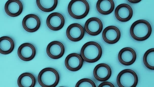 Bovenaanzicht van zwart elastische rubberen pakkingen met een ronde geometrische vorm op een gekleurde blauwe achtergrond. Rotatie. Samenvatting - Video