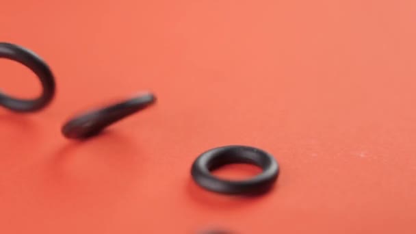 Afdichting rubber pakkingen vallen op een gekleurde oranje achtergrond in slow motion close-up. Hydraulische onderdelen. Rotatie - Video