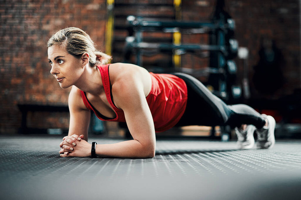 Holding it for as long as she can. Full length shot of an attractive young female athlete planking in the gym - Foto, afbeelding