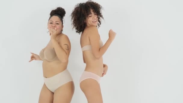 Šťastný jistý mladý asijské plus velikost žena ve spodním prádle tanec a zpěv s veselý fit African American přítelkyně proti bílému pozadí ve studiu - Záběry, video