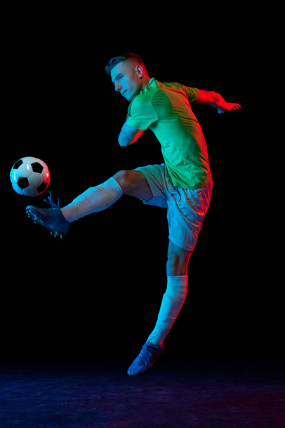 Goal. Young soccer, football player in motion and action with ball isolated on dark background in neon light. Concept of art, creativity, sport, energy. Copy space for ad, text - Φωτογραφία, εικόνα