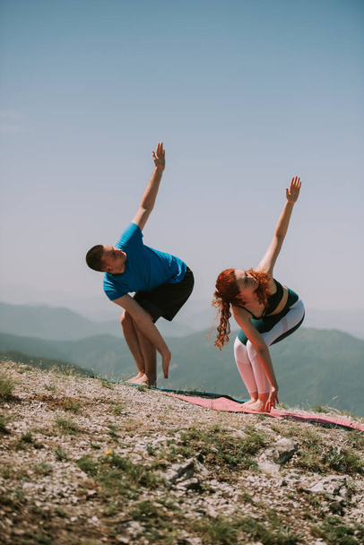 Yoga couple streching arms on the top of the mountain while standing on the yoga mats - Photo, Image