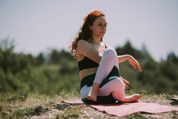 Beautiful red hair girl doing yoga at the top of the meadow - Fotoğraf, Görsel