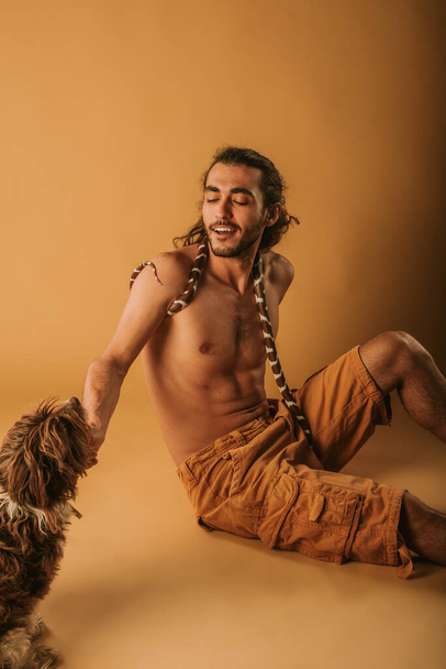 Jóképű férfi pózol a kaliforniai király kígyójával és gisz barna kutyájával a stúdióban. - Fotó, kép