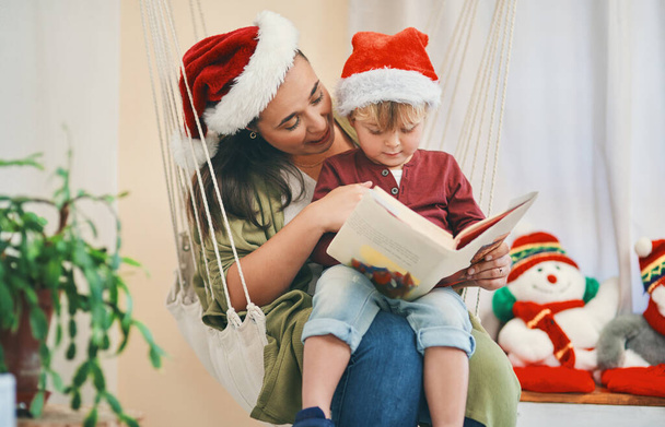 Όλα ήταν ήρεμα, όλα ήταν φωτεινά. Μια νεαρή γυναίκα διαβάζει ένα βιβλίο με τον αξιολάτρευτο γιο της τα Χριστούγεννα. - Φωτογραφία, εικόνα