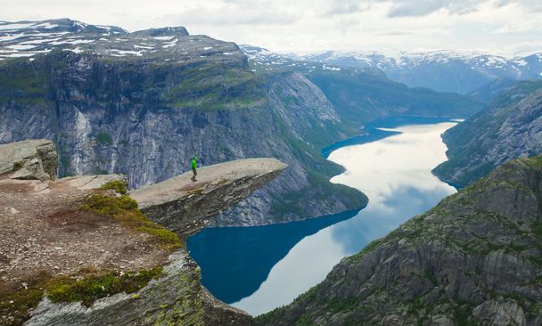 A vibrant picture of famous norwegian hiking place - trolltunga, the trolls tongue, rock skjegedall, with a tourist, and lake ringedalsvatnet and mountain panoramic scenery epic view, Norway - 写真・画像