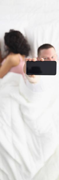 Вид зверху на чоловіка і жінку в ліжку, показує чорний екран смартфона, перевіряє гаджети вранці. Макет, копіювання простору, залежність від соціальних мереж, концепція доброго ранку
 - Фото, зображення