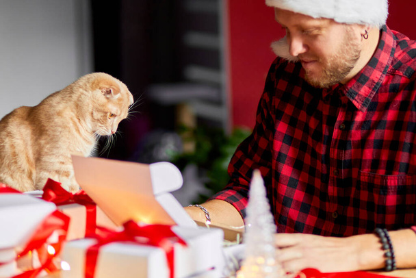 Vet Man in Santa hat and cat in hand making greeting card for New Year and Christmas, congratulation for clients or friends or family , packing presents or gifts, mail manager concept. - Foto, imagen