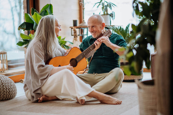 Senior couple playing on guitair, sitting in a cozy living room and enjoying autumn day. - Foto, Bild