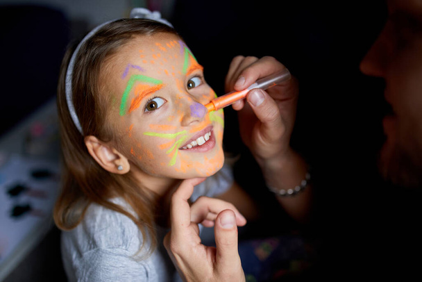 Daughter and father paint a face, having fun, leisure together at home on the sofa, dark light, Fathers day, family creative activities. - Foto, Imagem
