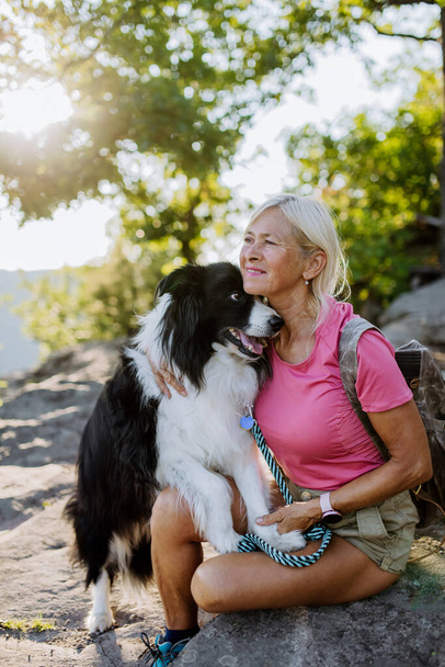 Senior woman resting and stroking her dog during walking in a forest. - Photo, Image