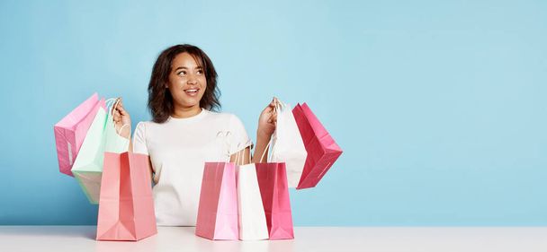Portrait of happy young woman with many shopping bags isolated over blue background. Concept of shopping, online order and delivery, Black Friday sales. Copy space for ad, text. Flyer - 写真・画像