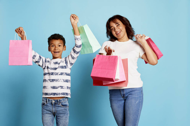 Portrait of cheerful woman and teen boy holding many shopping boxes isolated over blue background. Concept of shopping, online order and delivery, Black Friday sales. Copy space for ad, text - Foto, immagini