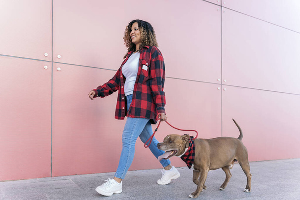 Smiley black woman with curly hair walking her dog in the street and having fun. - Foto, Imagen