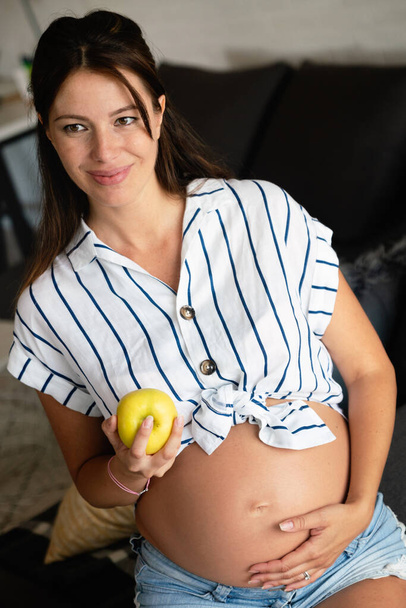 Pregnancy, healthy food and people concept Happy young pregnant woman eating apple. healthy food. - Фото, изображение