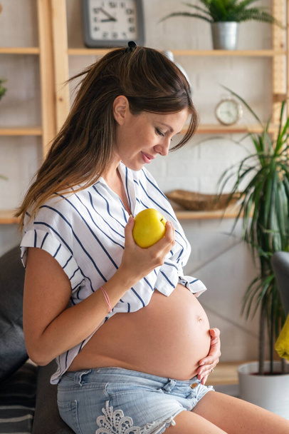 Pregnancy, rest, people and expectation concept. Happy beautiful pregnant woman touching her belly at home - Foto, Imagem