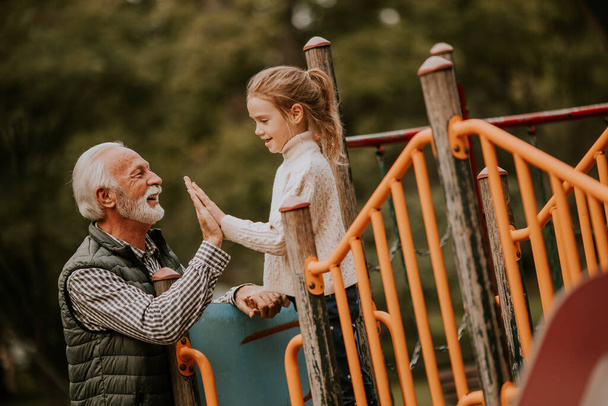 Schöner Opa verbringt am Herbsttag Zeit mit seiner Enkelin auf dem Spielplatz im Park - Foto, Bild