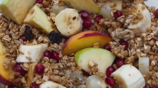 Natural crispy granola with fresh juicy fruits preparing for healthy breakfast close up. Baked sweet flakes with pieces banana apple apricot pomegranate in super slow motion. Vegetarian nutrition. - Footage, Video