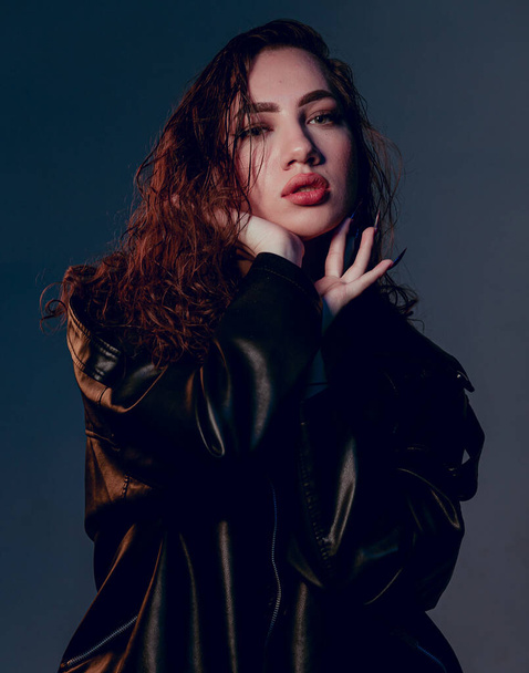 Plus size woman in black leather jacket. Beautiful curvy body, seductive lady posing In underwear. Attractive oversized female In lingerie standing on dark blue studio background. - Valokuva, kuva
