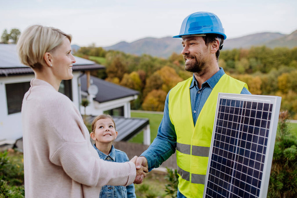 Smiling handyman, photovoltaics panels installer shaking hand with family owner of the house. - Φωτογραφία, εικόνα