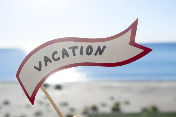 Stick with paper speech bubble with words Vacation on background sea, sky, sandy beach on a sunny summer day. Text-balloons with text from letters. Concept, symbol, sign vacation travel tourism rest. - Photo, Image