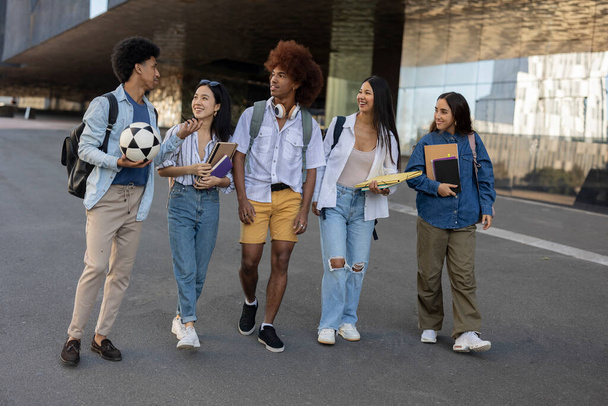 Wielorasowa zróżnicowana grupa uczniów z książkami spacerującymi po ulicach, wracającymi do domu po zajęciach i towarzyskimi - Zdjęcie, obraz