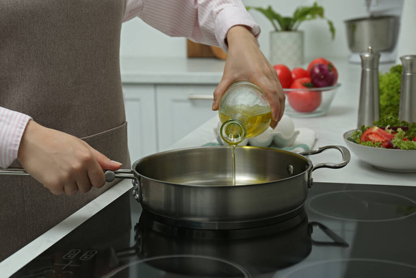 Woman pouring oil from jug into pan in kitchen, closeup - Fotoğraf, Görsel