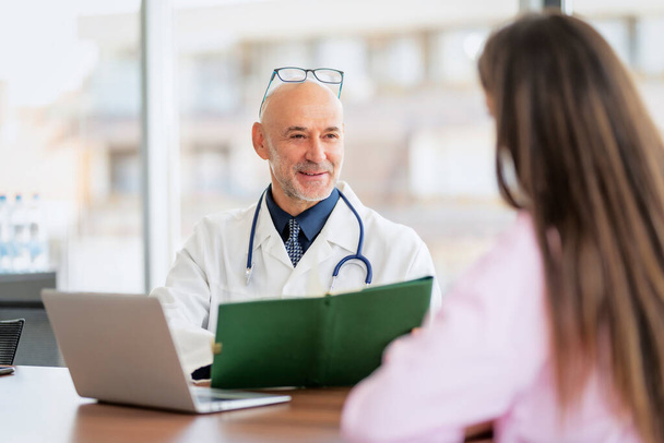 Shot of a male doctor explaining female patient while sitting in office behind a laptop. - Foto, afbeelding