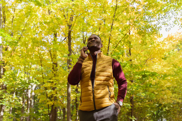 Ritratto di uomo afroamericano sorridente che parla al cellulare fuori nel parco autunnale - concetto di comunicazione e tecnologie - Foto, immagini