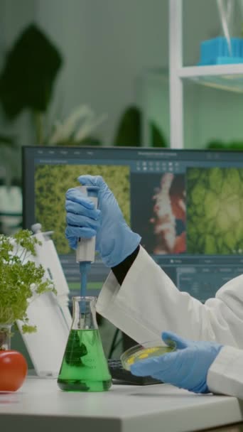 Вертикальное видео: ученый-биолог африканская женщина-исследователь берёт генетический раствор из пробирки с помощью микропипетки кладет в чашку Петри анализ гмо саженца, работающего в биологической лаборатории. - Кадры, видео