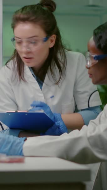 Vídeo vertical: Dos colegios revisando la muestra de carne vegana escribiendo experiencia en biotecnología después de un experimento químico. Científicos trabajando en sustitutos de carne vegetal en laboratorio de biología - Imágenes, Vídeo