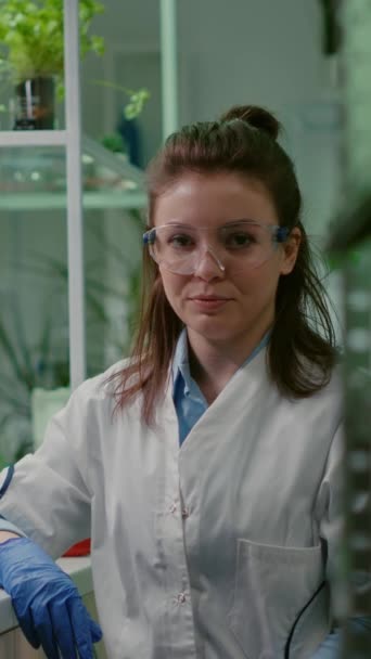 Vertical video: Portrait of chemist woman in white coat working in pharmaceutical laboratory. Biologist scientific analyzing organic plants genetically modified for engineering medical experiment, GMO - Footage, Video