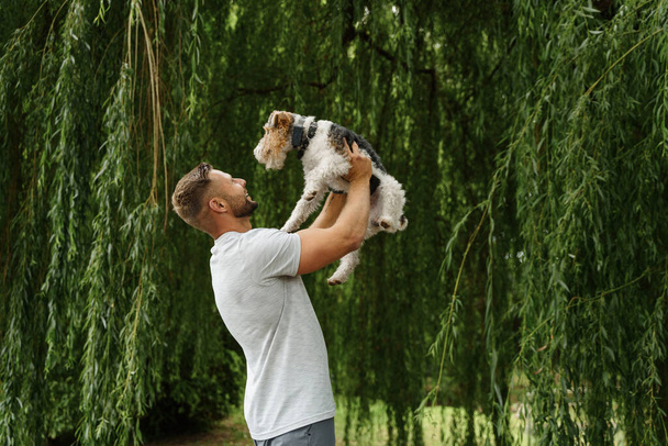 Portret van een blije man huisdier eigenaar met zijn mooie hondje in de natuur in het weekend. - Foto, afbeelding